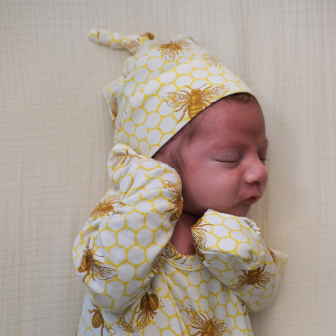 Newborn wearing a bamboo knotted hat with bees on it